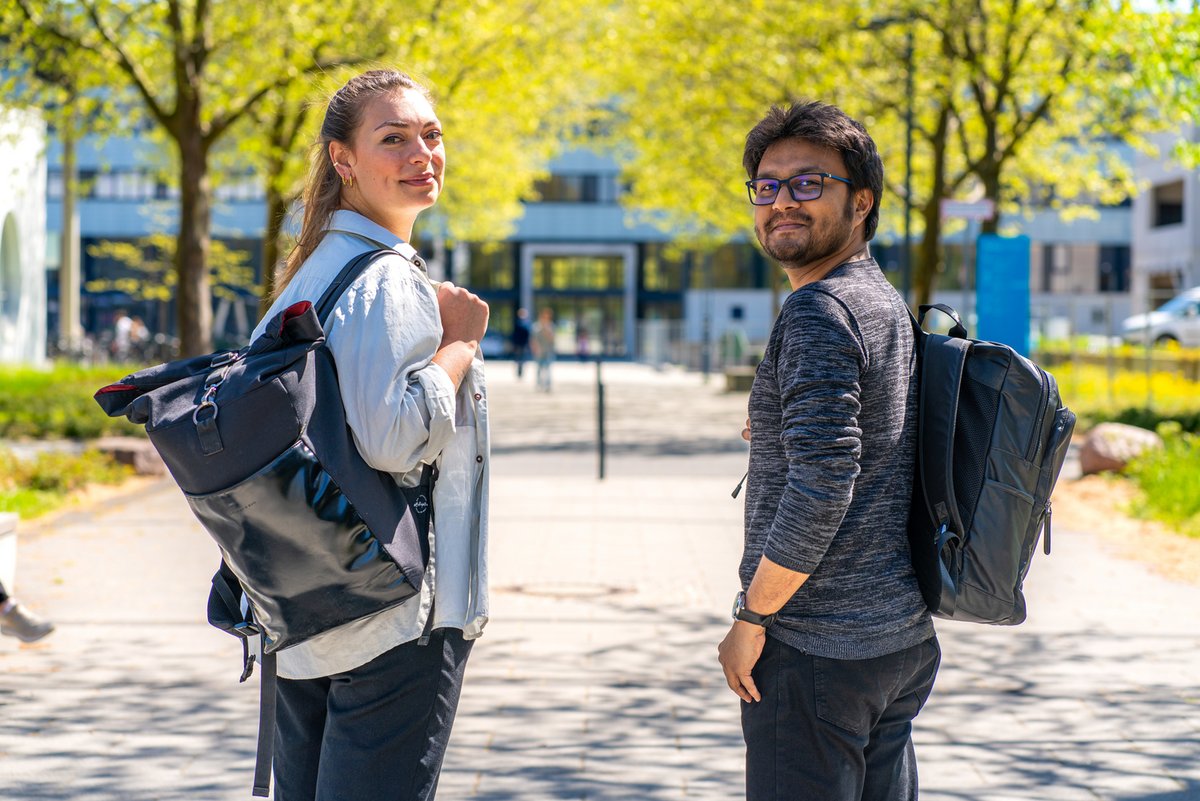 Studierende stehen auf der Konrad-Wachsmann-Allee und schauen in die Kamera. Im Hintergrund ist das Hauptgebäude zu sehen.